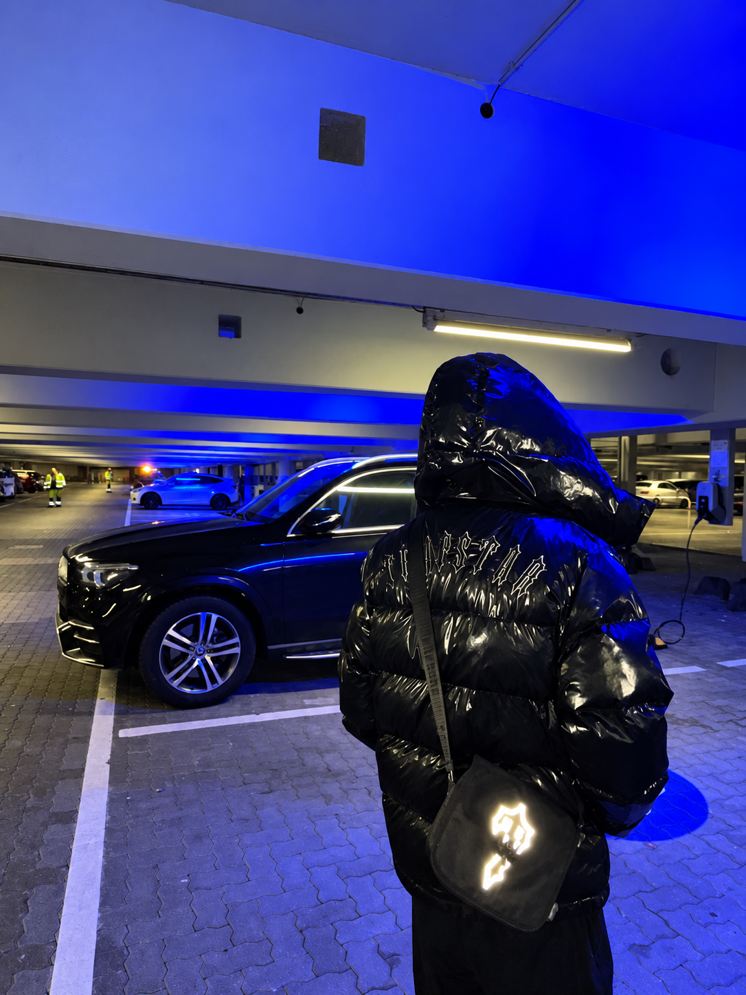 YGODOWN in a black hooded jacket beside a black SUV in a blue-lit garage